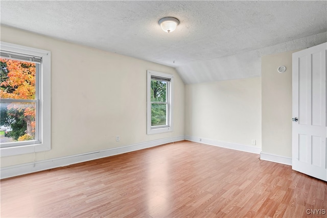 spare room featuring light hardwood / wood-style floors, a textured ceiling, and lofted ceiling