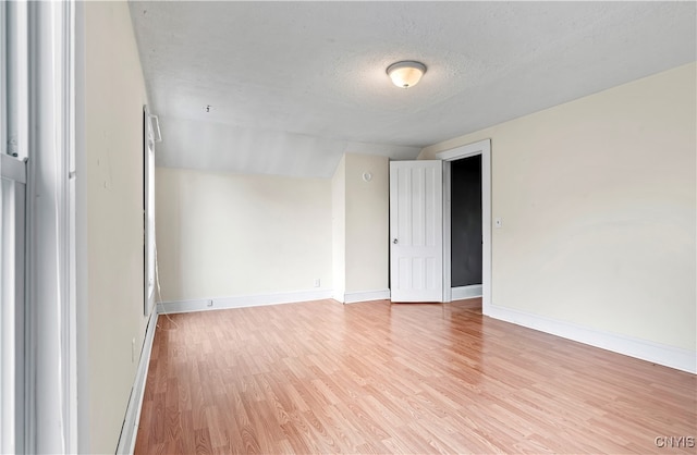 spare room featuring light hardwood / wood-style floors, a textured ceiling, and vaulted ceiling