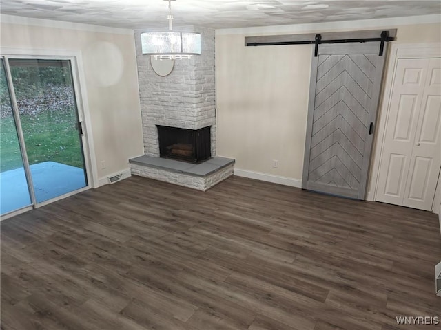 unfurnished living room with dark wood-type flooring, visible vents, a stone fireplace, and a barn door