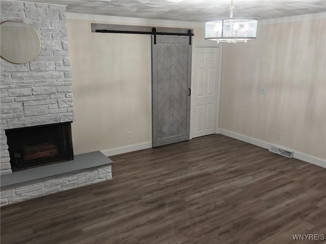 unfurnished living room with dark wood finished floors, a fireplace, visible vents, a barn door, and baseboards