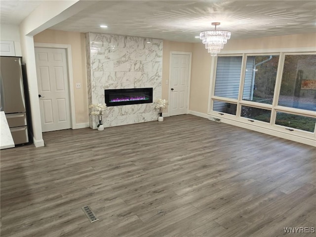 unfurnished living room featuring visible vents, baseboards, dark wood finished floors, a notable chandelier, and a high end fireplace