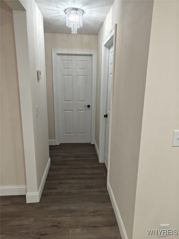 hallway with a chandelier, dark wood-type flooring, and baseboards