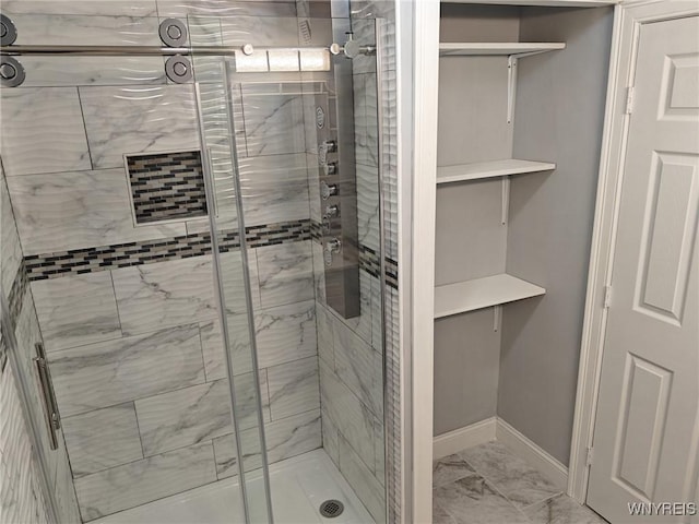 bathroom featuring marble finish floor, a shower stall, and baseboards