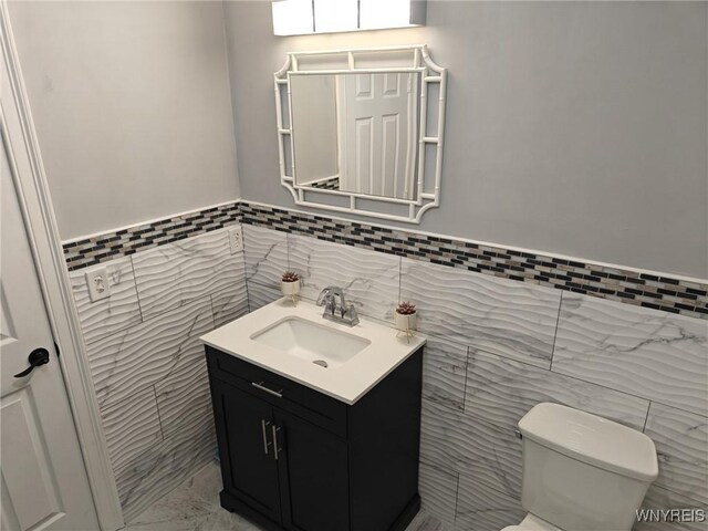 bathroom featuring toilet, vanity, and tile walls