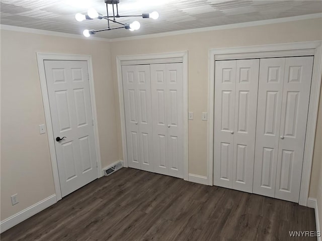 unfurnished bedroom featuring dark wood-style floors, multiple closets, visible vents, an inviting chandelier, and baseboards