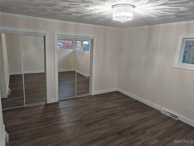 unfurnished bedroom with visible vents, dark wood-style flooring, crown molding, a chandelier, and multiple closets