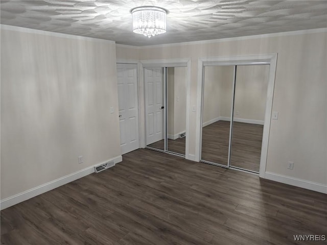 unfurnished bedroom with dark wood finished floors, two closets, visible vents, and crown molding