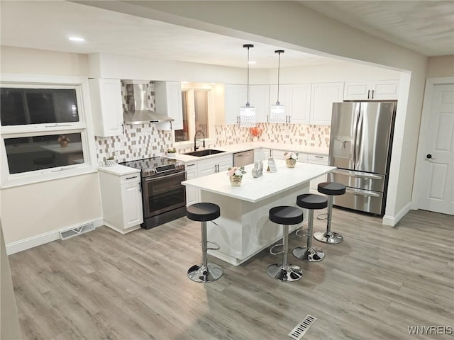 kitchen with wall chimney exhaust hood, stainless steel appliances, light countertops, and decorative light fixtures