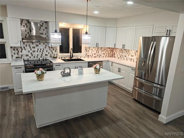 kitchen with light stone counters, decorative light fixtures, stainless steel appliances, wall chimney range hood, and a sink