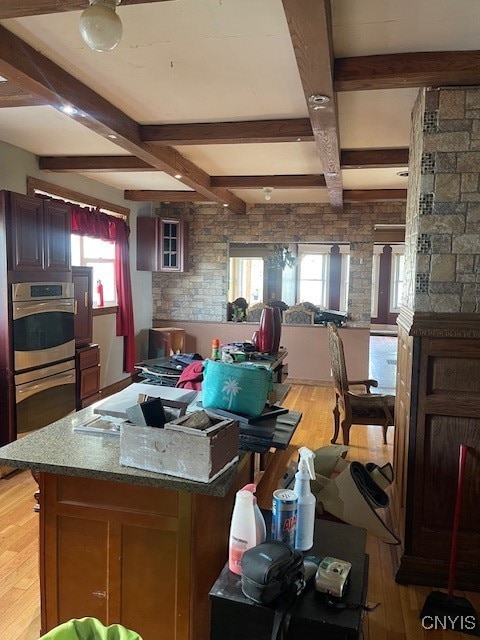 kitchen featuring beam ceiling, light hardwood / wood-style flooring, double oven, and a center island