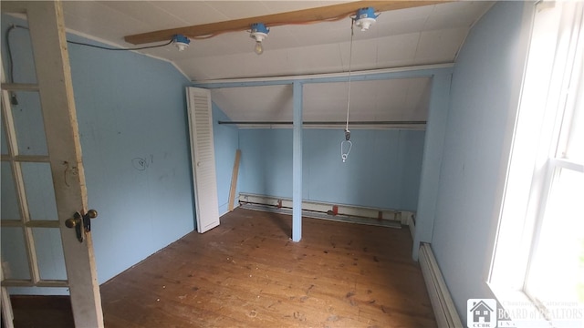 unfurnished bedroom with baseboard heating, lofted ceiling, wood-type flooring, and a closet