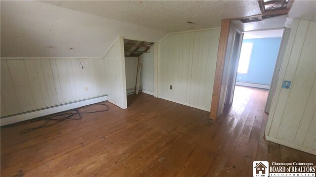 additional living space with lofted ceiling, dark wood-type flooring, a baseboard heating unit, and wood walls