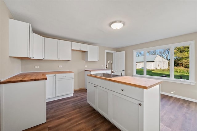 kitchen featuring butcher block counters, sink, white cabinetry, and an island with sink