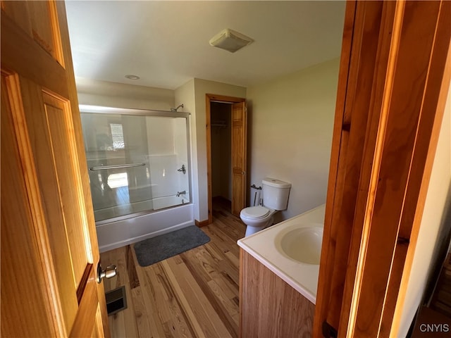 full bathroom featuring vanity, bath / shower combo with glass door, hardwood / wood-style flooring, and toilet