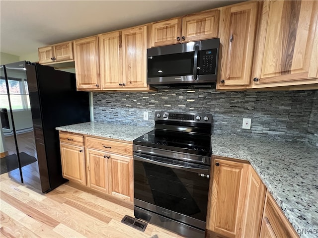 kitchen with light stone counters, appliances with stainless steel finishes, light hardwood / wood-style flooring, and backsplash