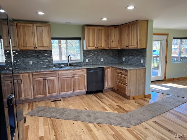 kitchen featuring decorative backsplash, black dishwasher, light wood-type flooring, dark stone countertops, and sink