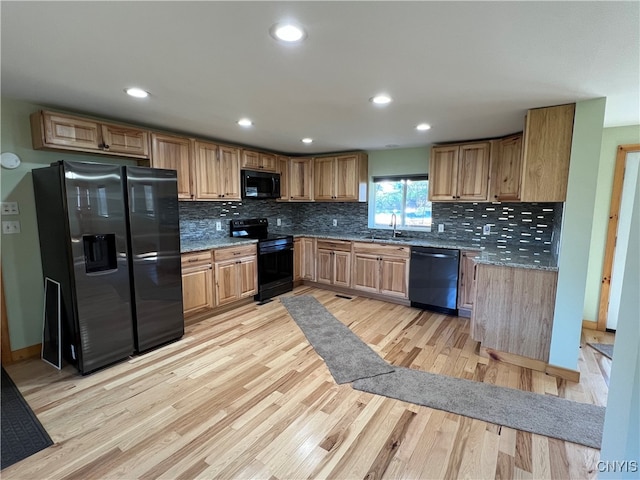 kitchen featuring dark stone countertops, backsplash, black appliances, and light hardwood / wood-style flooring