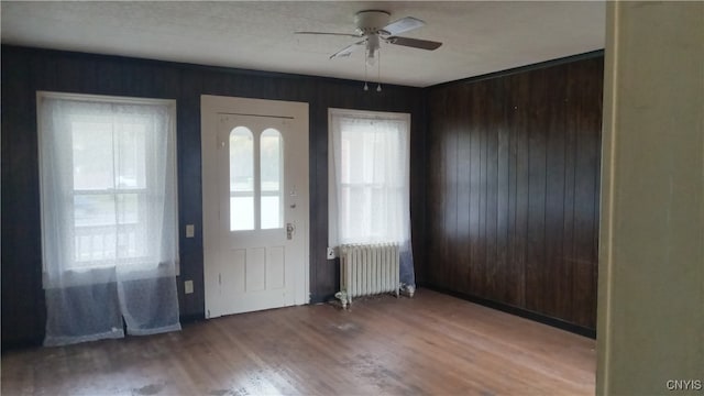 foyer with ceiling fan, hardwood / wood-style flooring, radiator heating unit, and wood walls