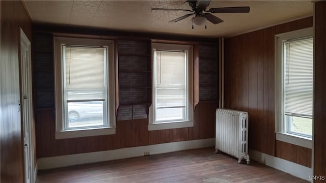 empty room featuring radiator, ceiling fan, wooden walls, and hardwood / wood-style floors