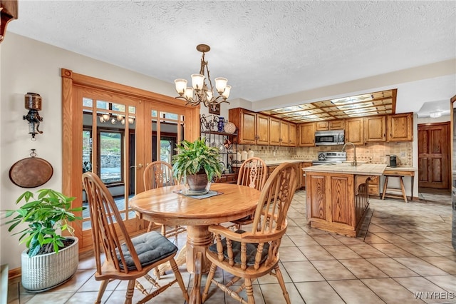 tiled dining space with a textured ceiling, a chandelier, and sink