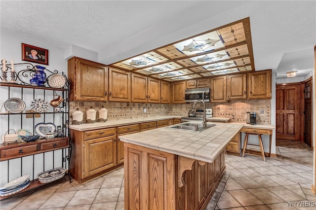 kitchen with light tile patterned flooring, a skylight, an island with sink, and tile counters