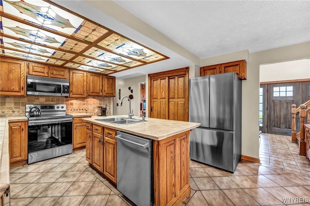 kitchen featuring sink, stainless steel appliances, decorative backsplash, light tile patterned floors, and a center island with sink