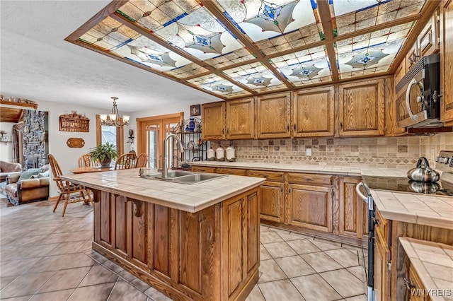 kitchen with tile counters, stainless steel appliances, a center island with sink, sink, and pendant lighting