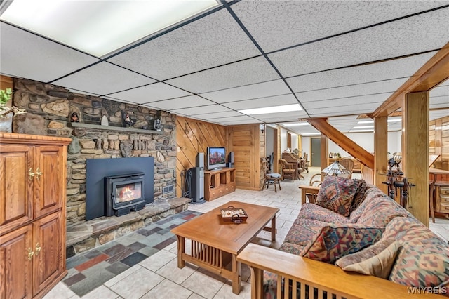 living room with a paneled ceiling, a wood stove, and wood walls