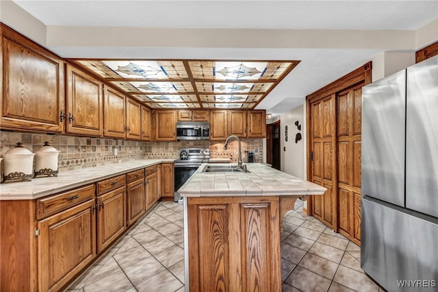 kitchen with appliances with stainless steel finishes, a skylight, sink, an island with sink, and tile counters