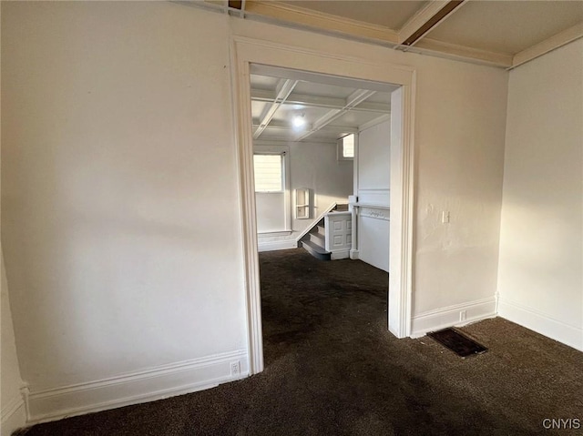 corridor featuring beam ceiling, coffered ceiling, and dark colored carpet