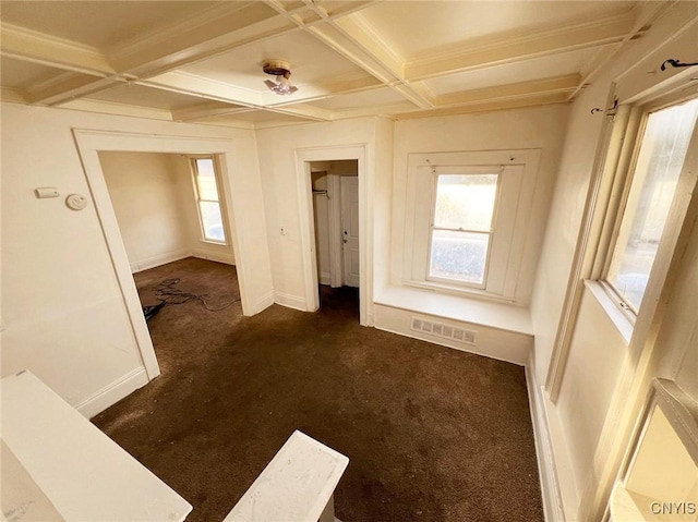 empty room with beam ceiling, a wealth of natural light, coffered ceiling, and dark colored carpet