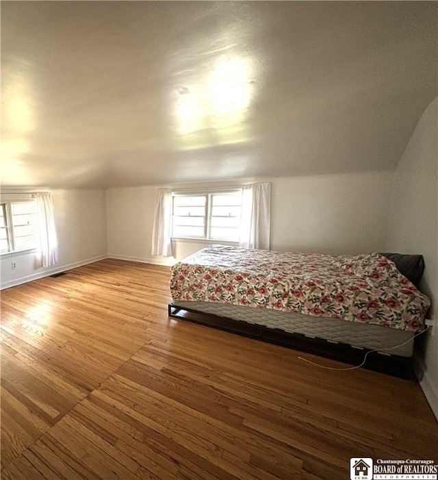 unfurnished bedroom featuring multiple windows, light wood-type flooring, and lofted ceiling