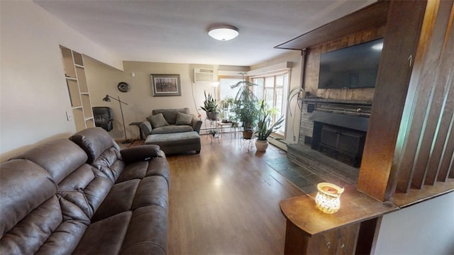 living room with an AC wall unit, a stone fireplace, and hardwood / wood-style flooring