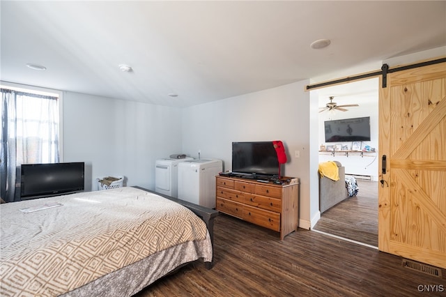 bedroom with a barn door, a baseboard heating unit, washing machine and dryer, and dark hardwood / wood-style floors