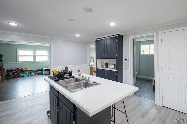 kitchen featuring a center island with sink, a kitchen bar, ornamental molding, light hardwood / wood-style floors, and sink