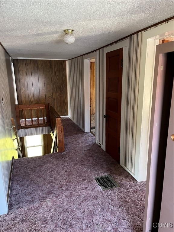 hall with carpet floors, a textured ceiling, and wooden walls