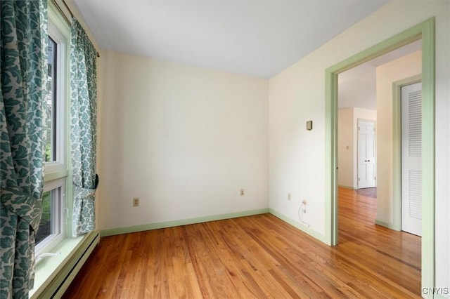 spare room with a healthy amount of sunlight, a baseboard heating unit, and light hardwood / wood-style floors