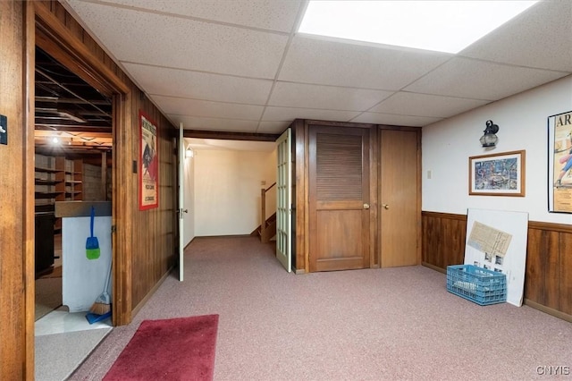 interior space with a drop ceiling, light carpet, and wood walls