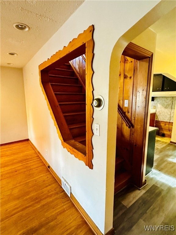 staircase with a textured ceiling and wood-type flooring