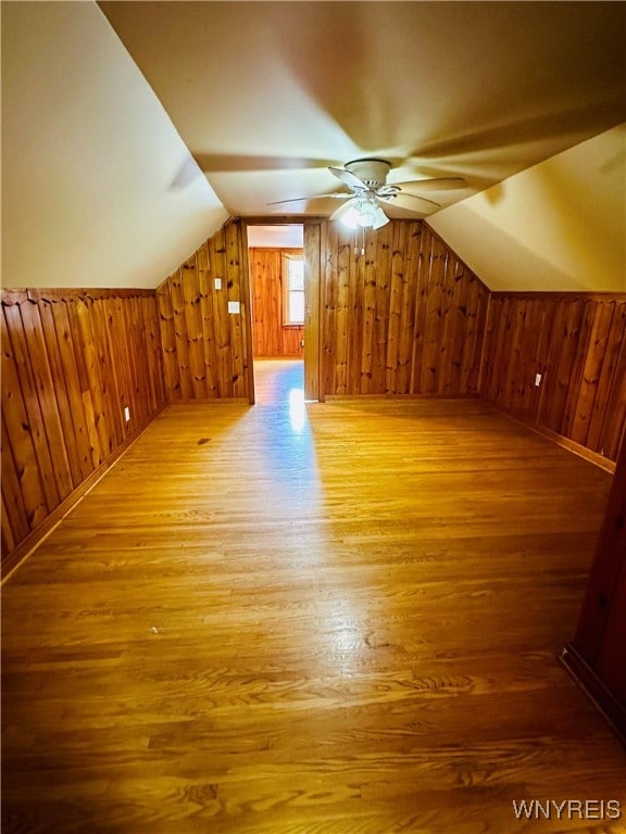 bonus room with wood walls, hardwood / wood-style floors, vaulted ceiling, and ceiling fan