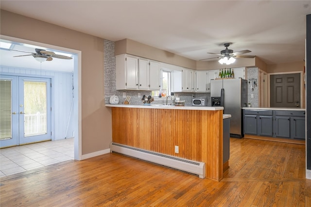 kitchen with stainless steel fridge, a baseboard heating unit, kitchen peninsula, and light hardwood / wood-style floors