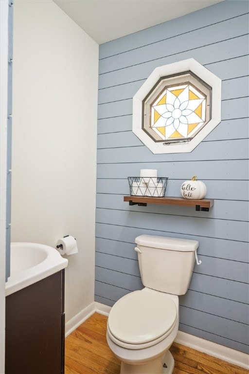 bathroom featuring toilet, vanity, wood-type flooring, and wooden walls