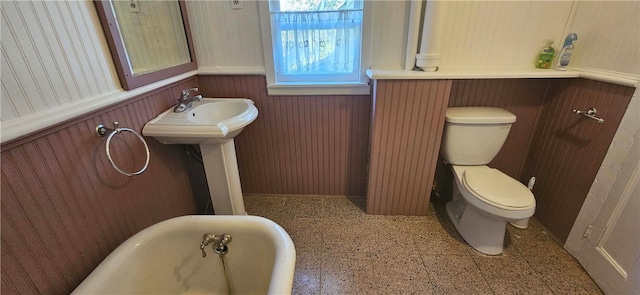 bathroom featuring wooden walls, toilet, and a washtub