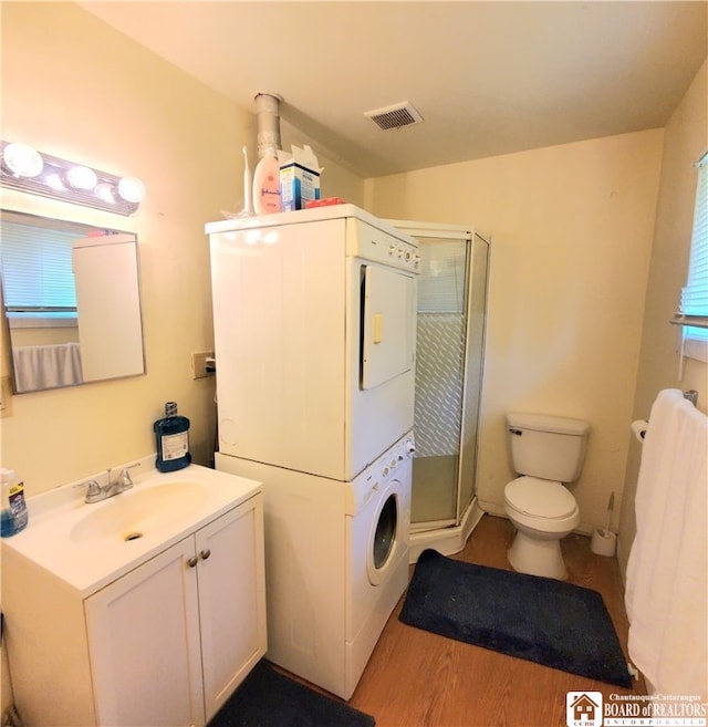 bathroom with hardwood / wood-style flooring, toilet, stacked washer / drying machine, vanity, and an enclosed shower