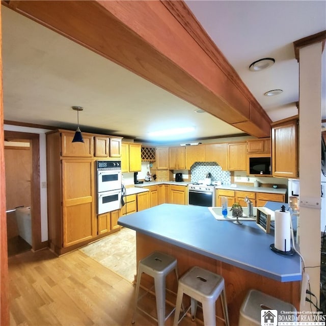 kitchen featuring tasteful backsplash, hanging light fixtures, light hardwood / wood-style flooring, double oven, and electric range oven