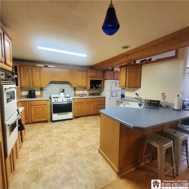 kitchen featuring kitchen peninsula, a breakfast bar area, pendant lighting, sink, and white appliances