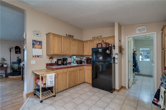 kitchen with black fridge, tile counters, vaulted ceiling, and a textured ceiling