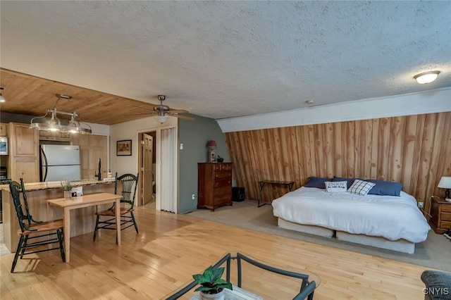 bedroom featuring sink, a textured ceiling, light wood-type flooring, stainless steel refrigerator, and wooden walls