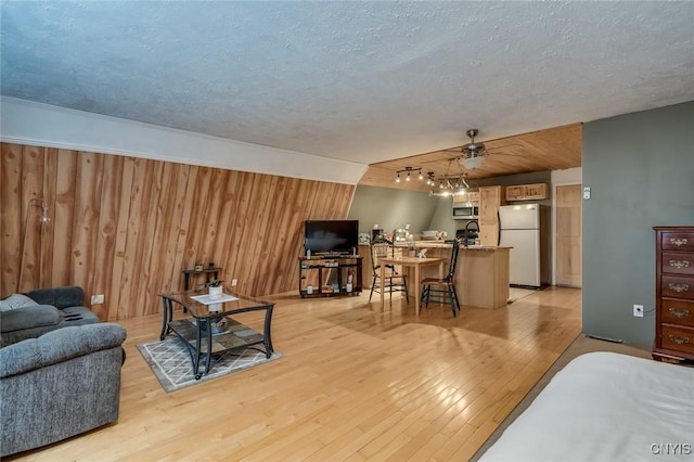 living room with ceiling fan, wooden walls, a textured ceiling, and light wood-type flooring