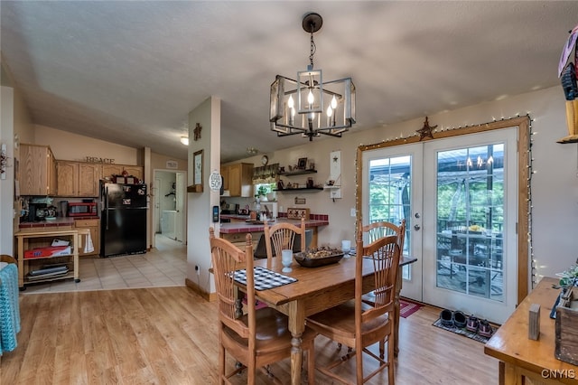 dining space with lofted ceiling, a notable chandelier, light wood-type flooring, and french doors